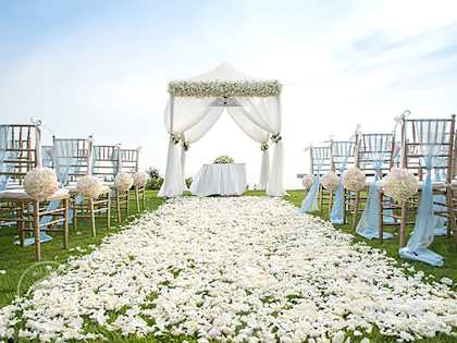 Outdoor wedding ceremony setup with white canopy tent, floral aisle décor, and chairs arranged on a green lawn
