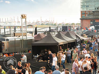 Outdoor food festival with black pop-up canopy tents and crowds enjoying BBQ vendors near the waterfront
